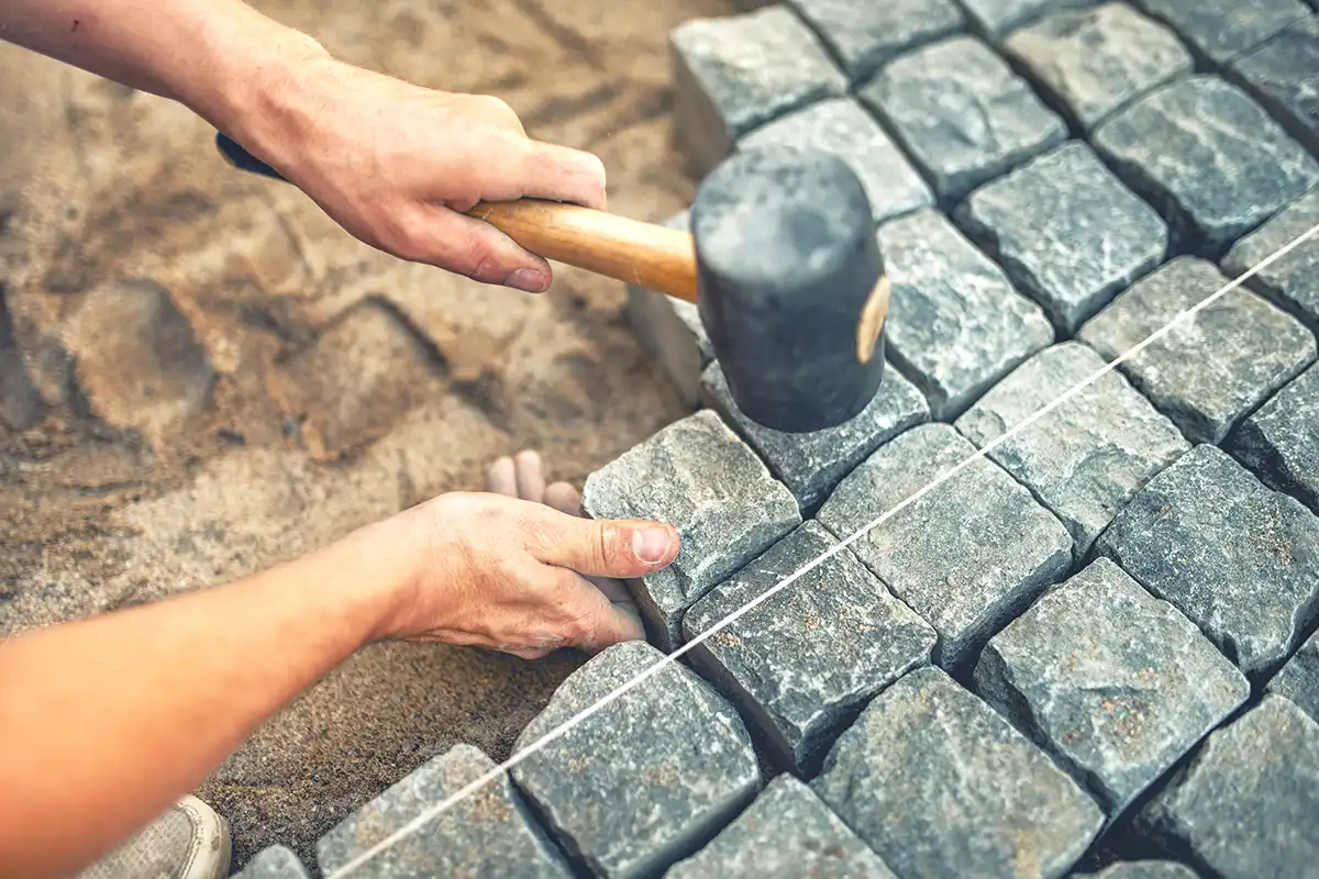 Mann arbeitet mit Hammer an Gestaltung Steinpfades Mann arbeitet mit Hammer an Gestaltung Steinpfades