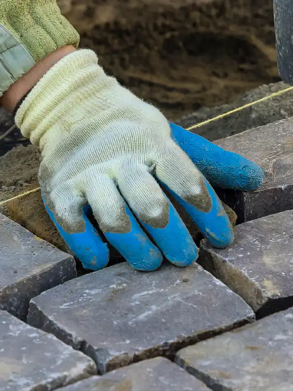 Mann mit blauen Handschuhen verlegt Pflastersteine